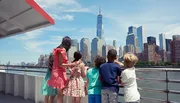 A group of children and an adult are enjoying a scenic view of the Manhattan skyline from a boat or waterfront.