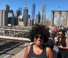A person is smiling for the camera on a sunny day with the Brooklyn Bridge and the New York City skyline in the background