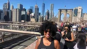 A person is smiling for the camera on a sunny day with the Brooklyn Bridge and the New York City skyline in the background.