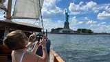 Passengers on a sailboat are capturing photos of the Statue of Liberty on a sunny day.