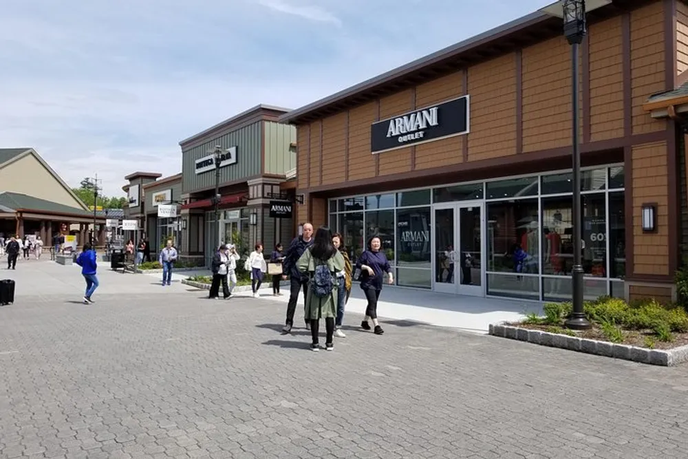 Shoppers walk through an outdoor outlet mall with the Armani Outlet store in the background