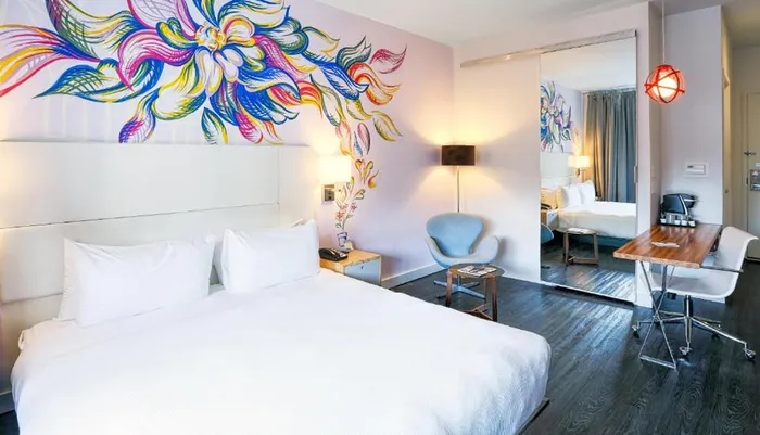 The image shows a modern hotel room with a vibrant floral wall mural sleek furniture and a comfortable ambiance