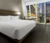 A modern hotel room with a large bed contemporary furnishings and a scenic view of a citys illuminated high-rise buildings through its wide window at night