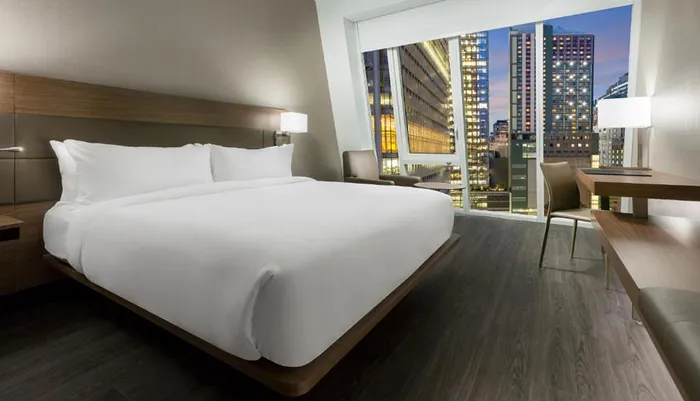 A modern hotel room with a large bed contemporary furnishings and a scenic view of a citys illuminated high-rise buildings through its wide window at night