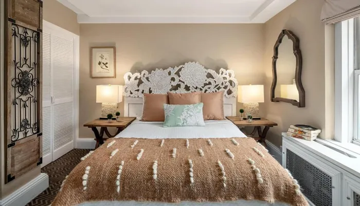 The image shows an elegantly decorated bedroom with a distinctive lace-like headboard symmetrical side tables with lamps and a cozy brown textured blanket on the bed