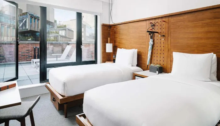 The image shows a modern hotel room with two twin beds wooden accents and a sliding glass door leading to a balcony