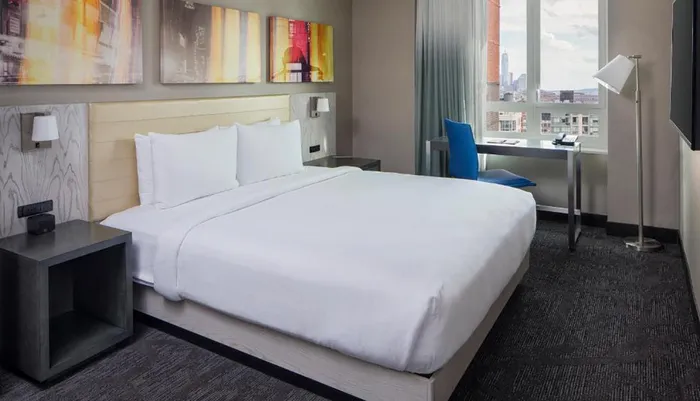 A modern hotel room with a large bed a wall-mounted art piece and a city view through the window