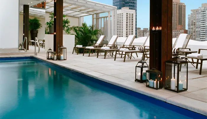 An urban rooftop pool area featuring lounge chairs and decorative lanterns with a skyline of high-rise buildings in the background