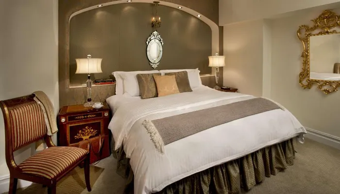 The image shows an elegantly decorated bedroom with a large bed ornate mirrors and antique-style furniture