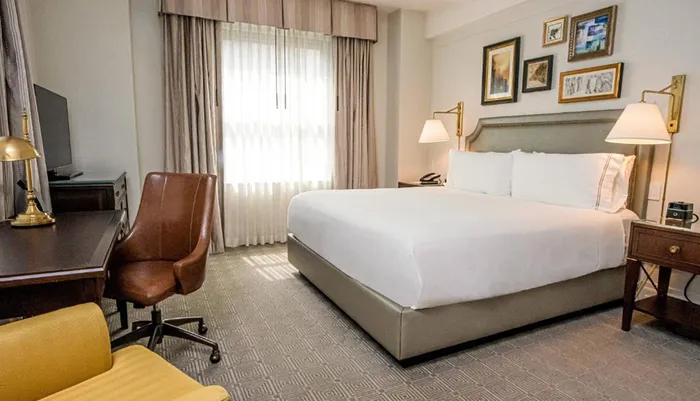 The image shows a neatly arranged hotel room with a large bed desk chair and wall decorations reflecting a comfortable and tidy guest accommodation