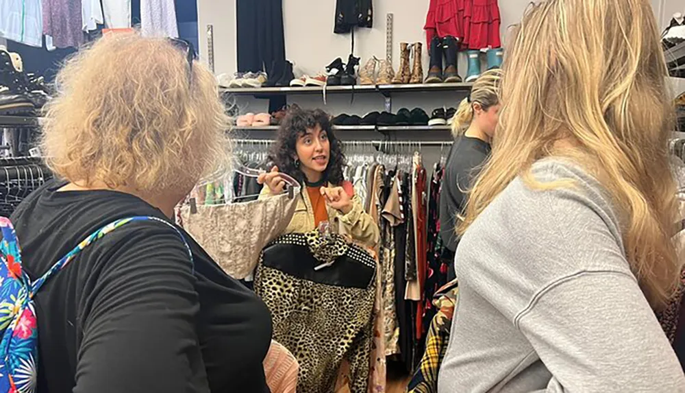 A group of people is shopping in a clothing store with one person in the center holding up a garment and seemingly engaging in a conversation with companions
