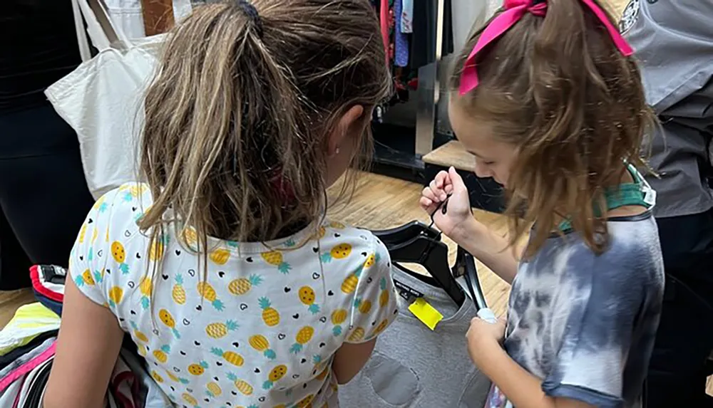 Two young children are looking intently at something on a clothes hanger in a store with one of them using a magnifying glass to examine it closely