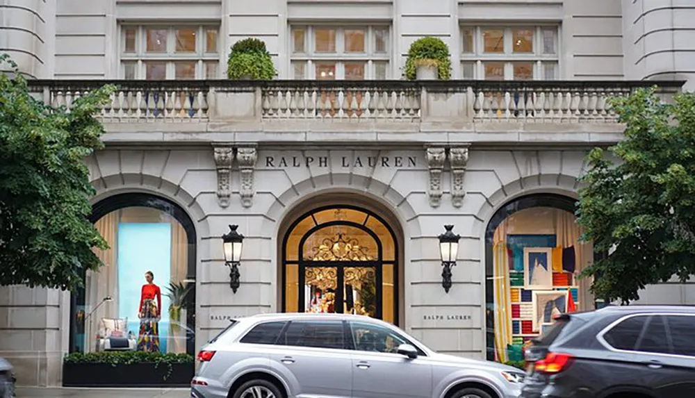 The image shows the facade of a Ralph Lauren store with an elegant archway and window displays and a passing car is partially visible in the foreground