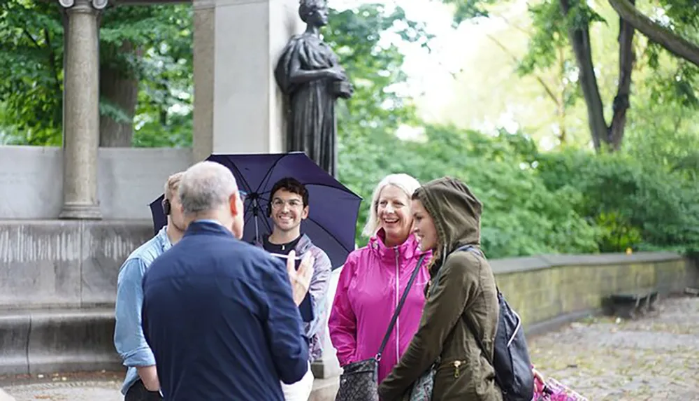 A group of people one holding an umbrella appear engaged and smiling during an outdoor conversation
