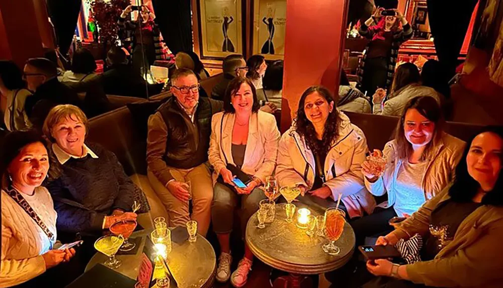A group of people are enjoying drinks and socializing at a warmly-lit indoor venue with an ambient background