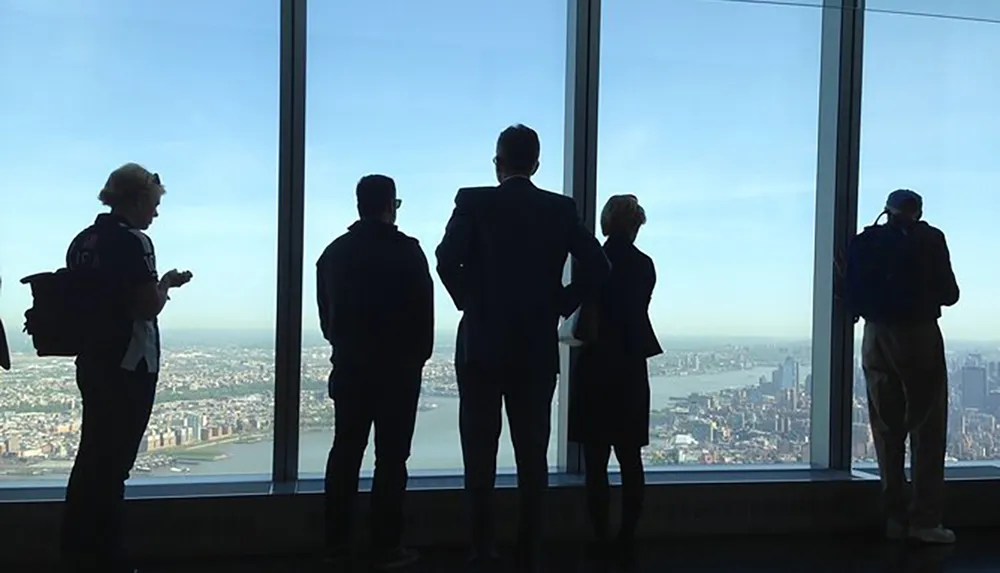 Five individuals are silhouetted against a large window overlooking a cityscape from a high vantage point