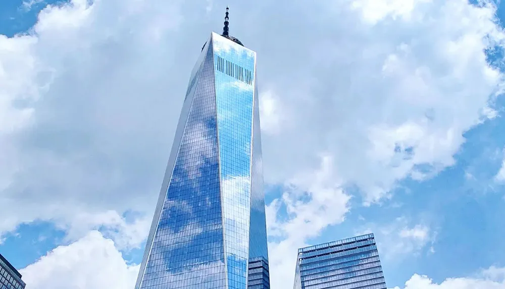 The image features the One World Trade Center skyscraper towering against a backdrop of blue sky and fluffy white clouds