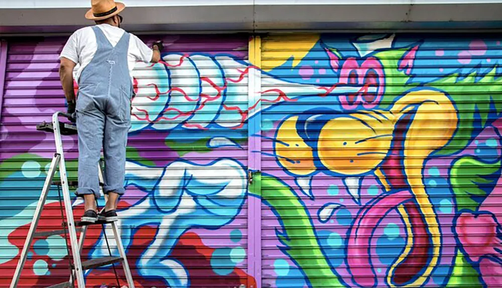 An artist is standing on a ladder while creating vibrant graffiti art on a roller shutter