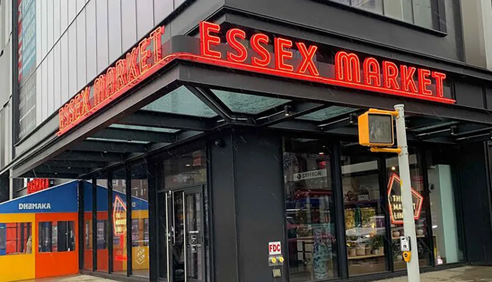 The image shows the exterior of Essex Market with a prominent red neon sign above the entrance on an overcast day