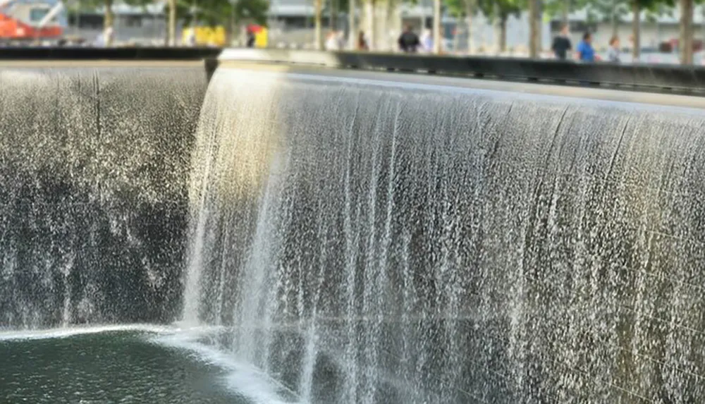 The image shows a man-made waterfall in an urban setting with water cascading smoothly down a curved wall into a pool below