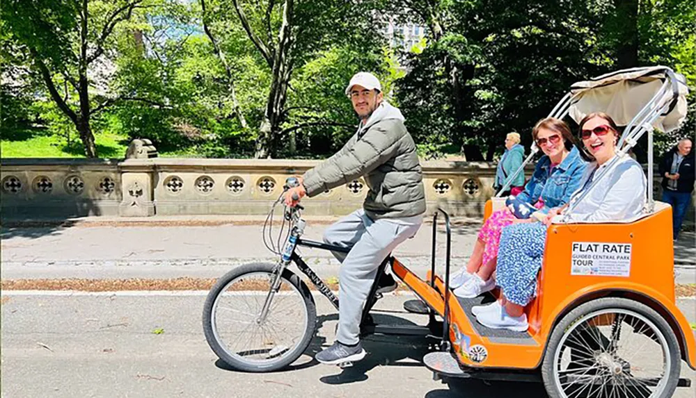 A pedicab driver is cycling with two passengers enjoying a ride in a sunny park setting