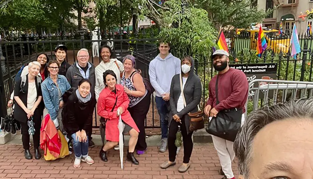 A diverse group of people is posing for a group photo outdoors with some individuals smiling and one person wearing a face mask