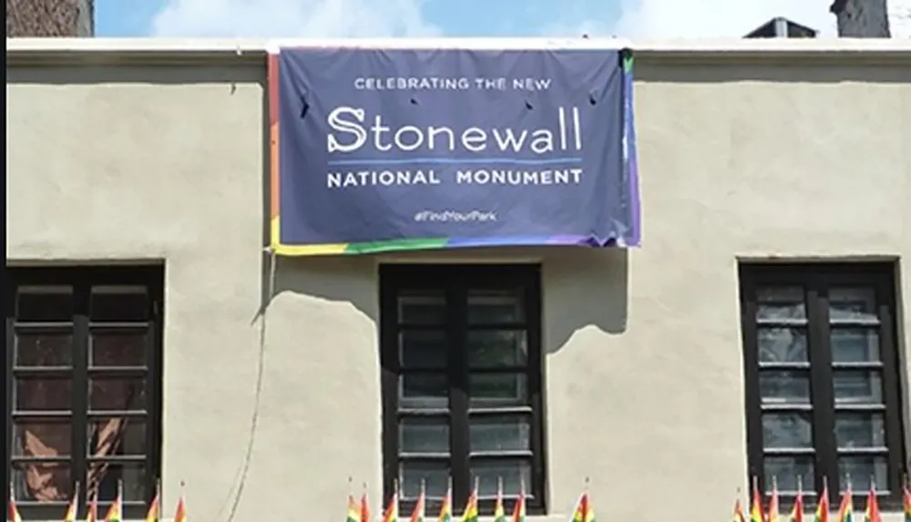 A banner hanging on a building celebrates the new Stonewall National Monument flanked by pride flags below