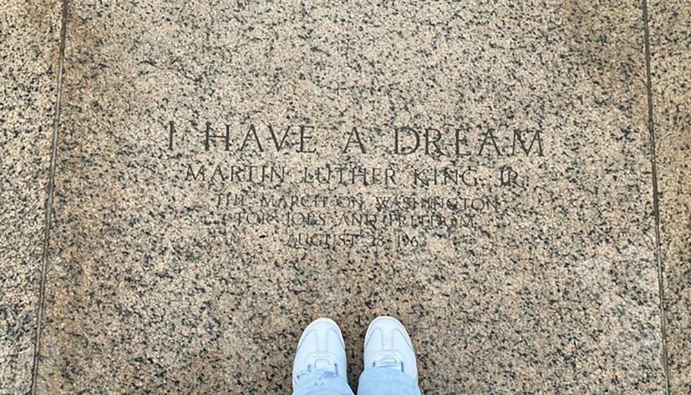 The image shows the I Have a Dream inscription from Martin Luther King Jrs historic speech at the Lincoln Memorial with someones feet at the bottom of the frame indicating a visitor paying respects or contemplating the site