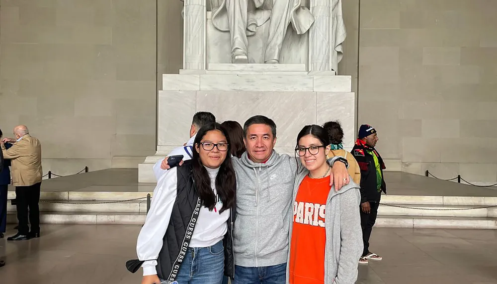 Three individuals are posing for a photo in front of the statue of Abraham Lincoln at the Lincoln Memorial in Washington DC