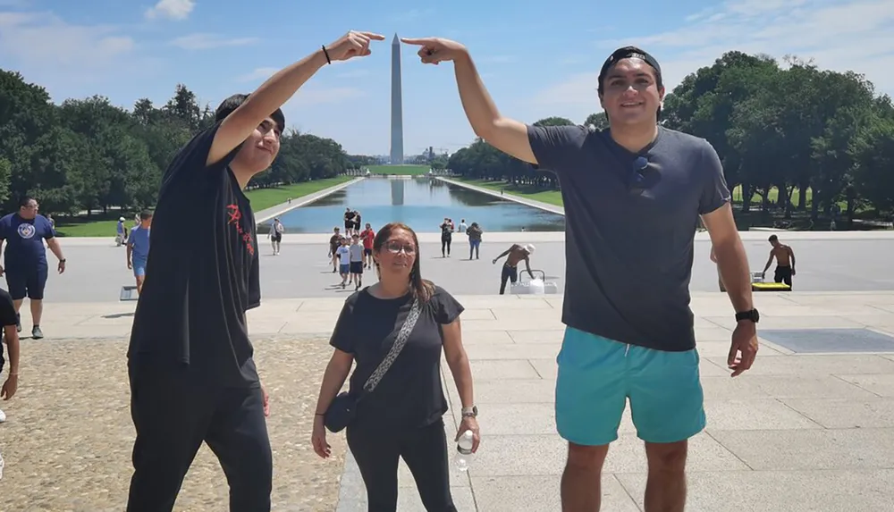 Two individuals are playfully touching the tip of the Washington Monument with their fingers while a third person stands between them at the National Mall