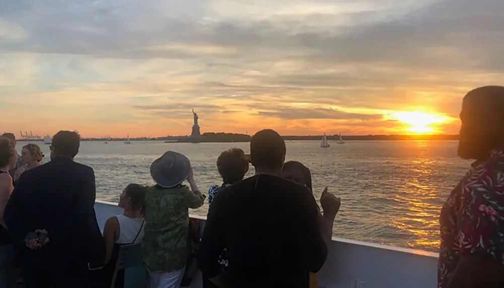 People on a boat are enjoying a beautiful sunset with the Statue of Liberty in the background