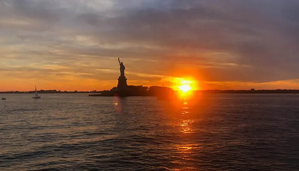 The image captures a stunning sunset behind the Statue of Liberty with vibrant colors reflecting on the water