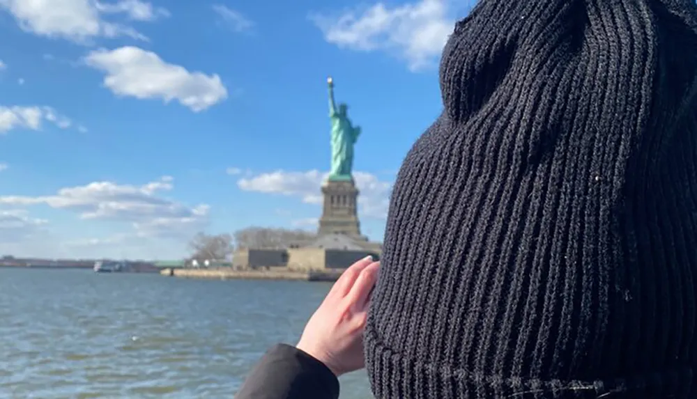 A person in a knit hat appears to be reaching out to the Statue of Liberty in the distance