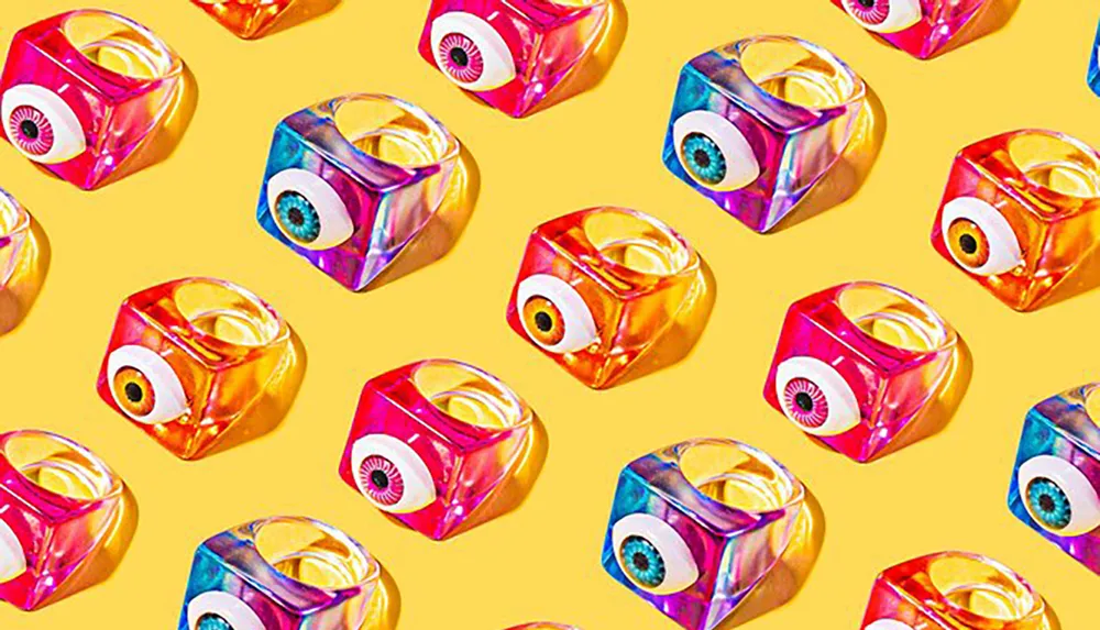 The image shows a pattern of colorful shiny cubes with stylized eyes on one side against a yellow background