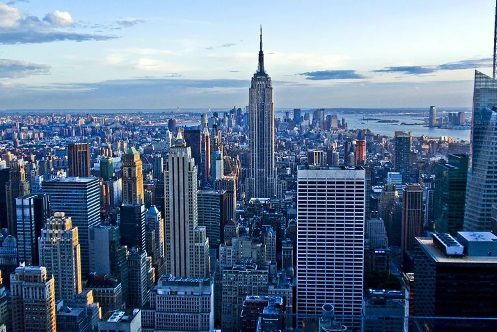 This image captures a panoramic view of New York Citys skyline with the Empire State Building prominently featured in the center during what appears to be late afternoon