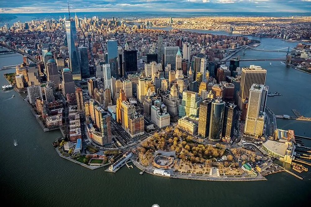 The image shows an aerial view of Lower Manhattan in New York City highlighting the dense skyscraper landscape with the One World Trade Center prominently visible against the backdrop of a setting sun