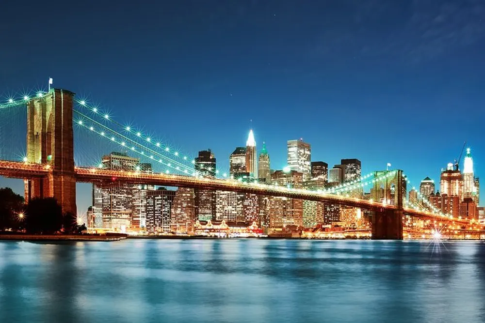The Brooklyn Bridge stands illuminated at night against the backdrop of the New York City skyline