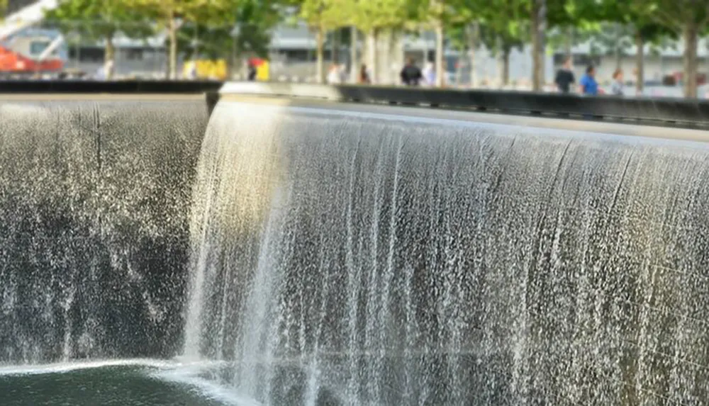 The image features a close-up of a cascading water fountain with blurred vegetation and people in the background