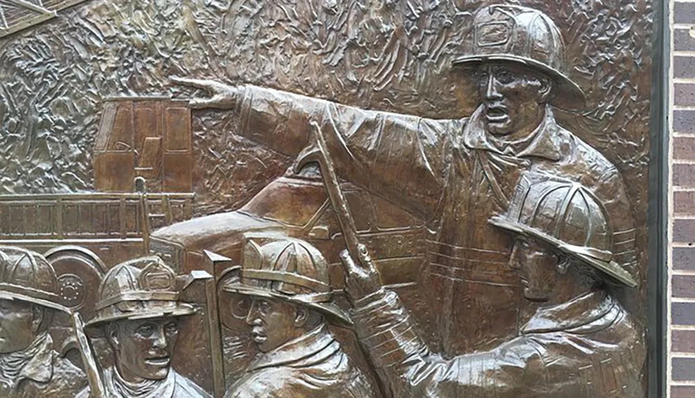 The image shows a bronze relief sculpture of firefighters in action with one prominently pointing in a direction