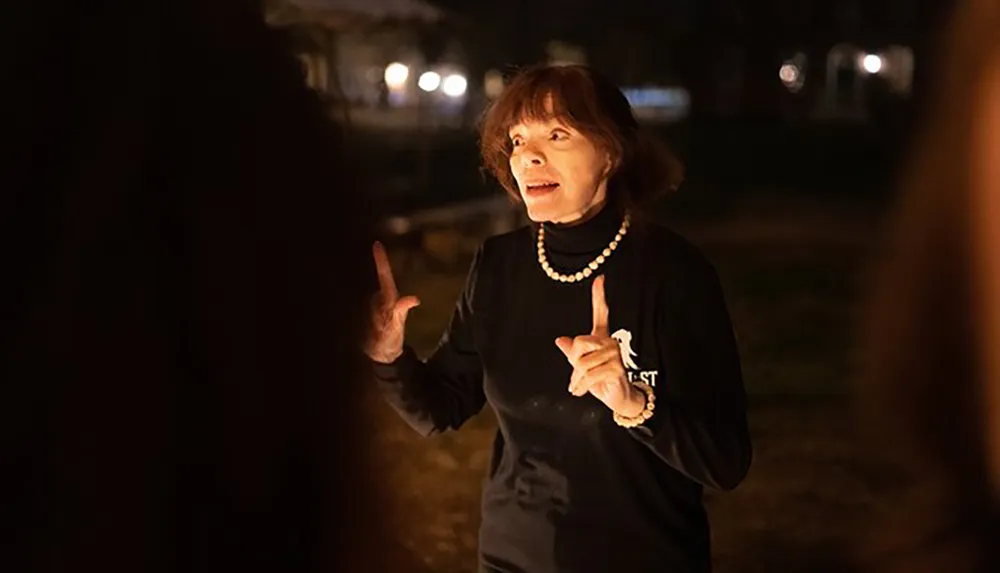 A woman is animatedly speaking outdoors at night possibly addressing a group while gesturing with her hands
