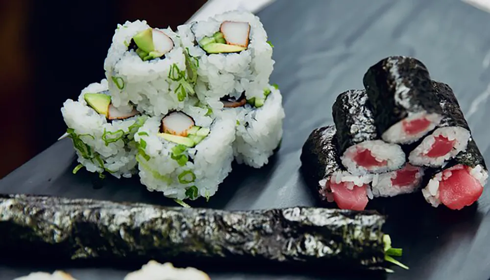 The image displays a variety of sushi rolls with different fillings arranged on a slate serving plate