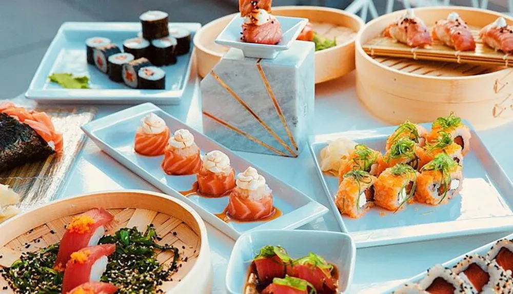 The image shows an assortment of beautifully presented sushi dishes on various plates and a bamboo steamer suggesting a fine dining experience