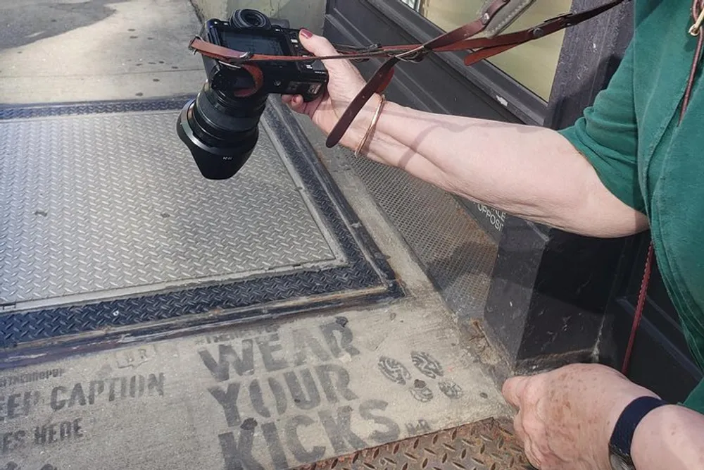 A person is holding a camera next to a dirty doormat with the phrase Wear your kicks stenciled on it