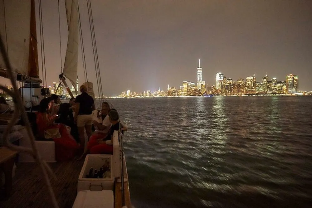 People are enjoying a nighttime sail with a view of a brightly lit city skyline in the background