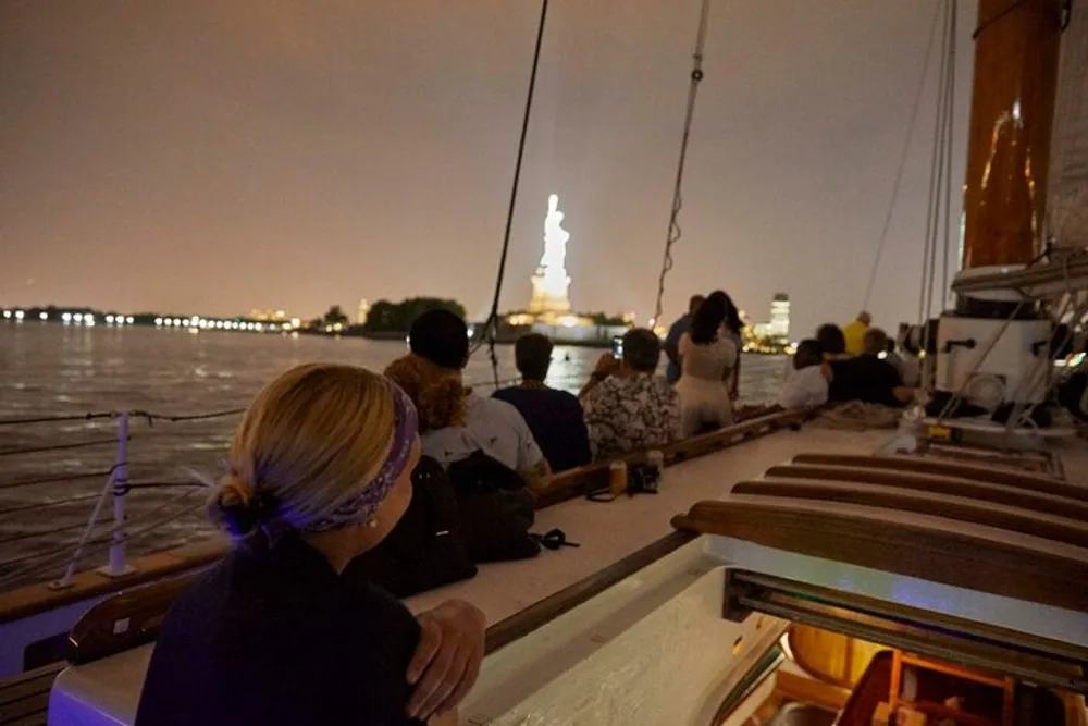 Passengers on a boat are enjoying a night-time view of the Statue of Liberty