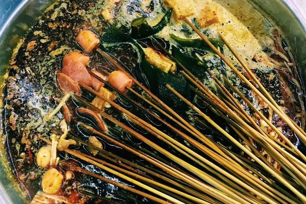 The image shows a variety of skewered foods cooking in a simmering hot pot with a diverse mix of spices and ingredients creating a colorful and potentially spicy broth