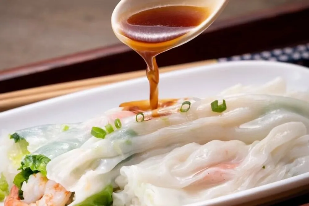 A close-up image of a dish of Asian-style dumplings with a spoon drizzling sauce over them