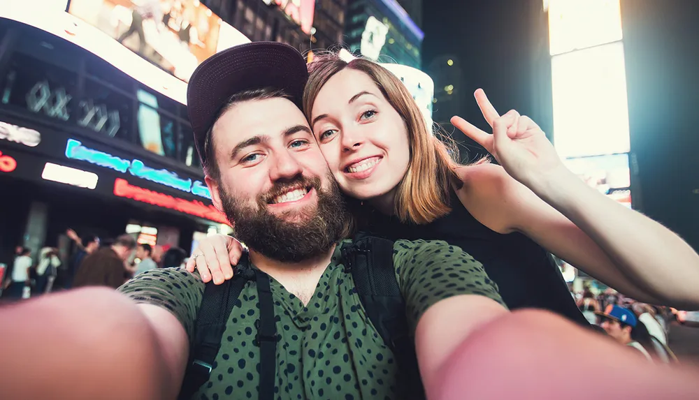 A cheerful couple is taking a selfie together in a brightly lit urban area at night