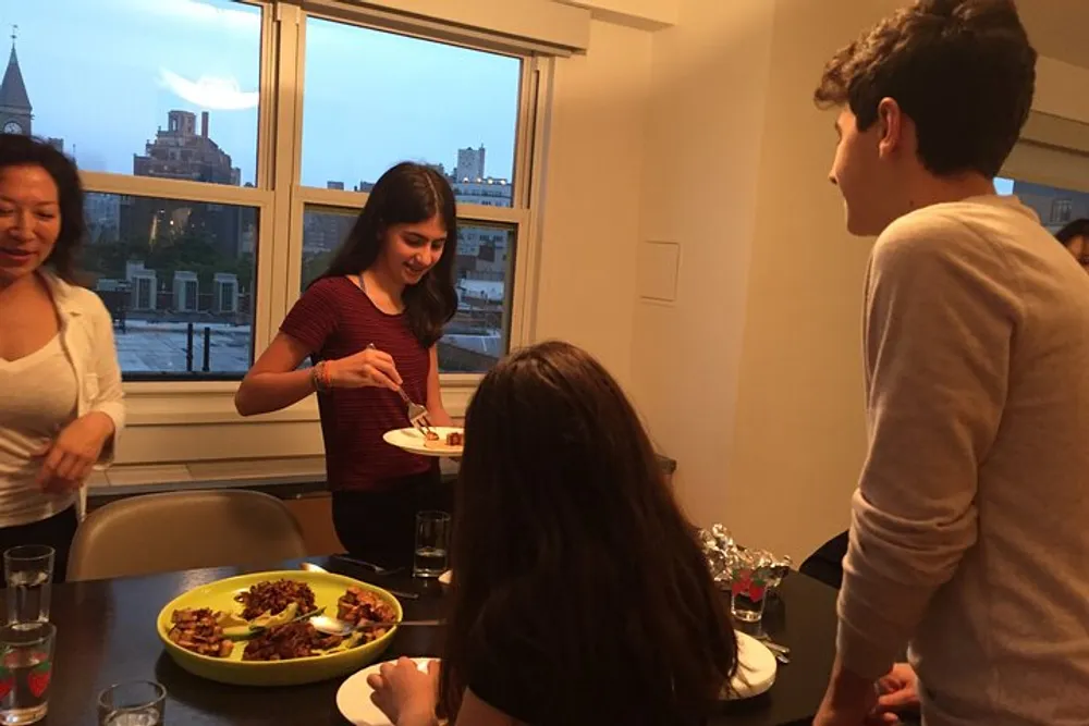 Several people are gathered around a dinner table with a plate of food in focus appearing to be enjoying a casual social gathering