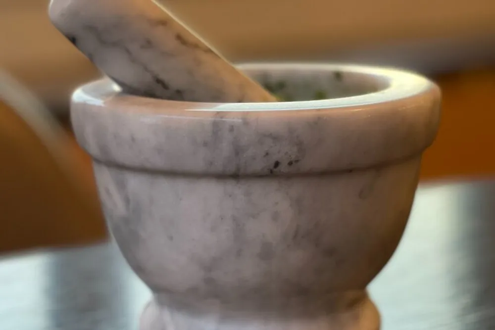 The image shows a close-up of a marble mortar and pestle on a table with a softly blurred background
